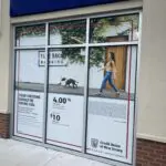 A woman walking her dog in front of a store window.