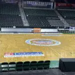A basketball court with seats and a logo on the floor.